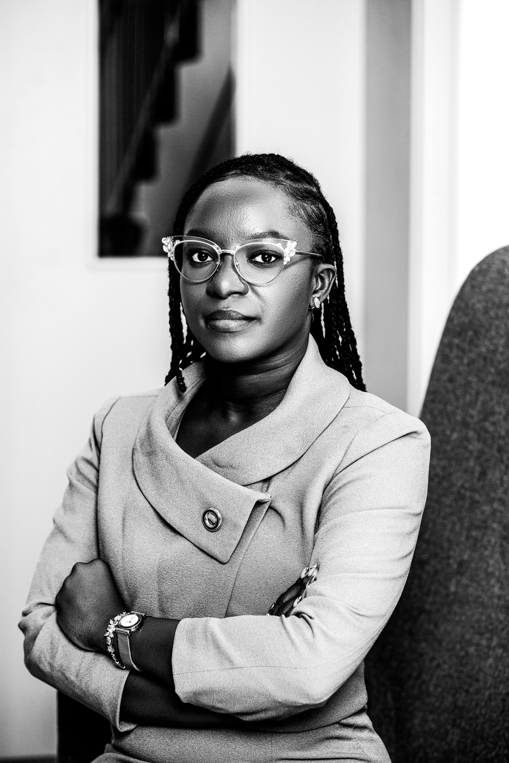 Elegant black and white portrait of a confident woman in office setting, arms crossed.