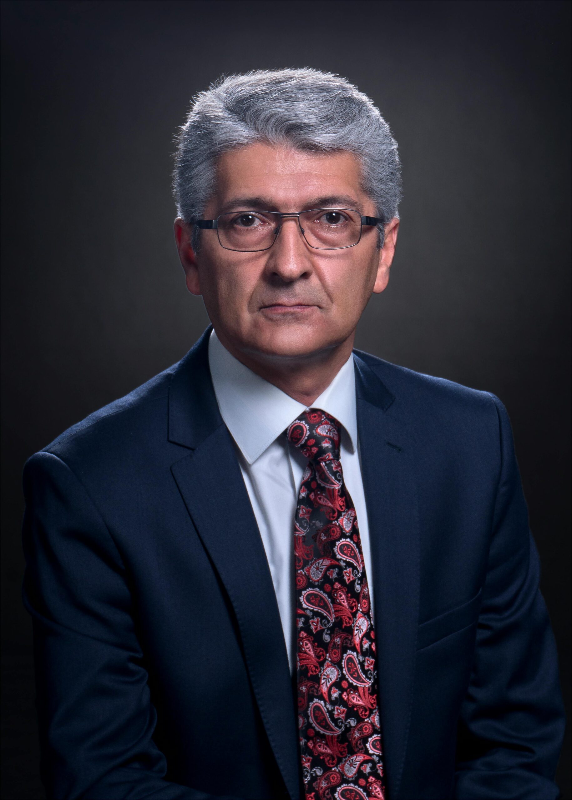 Studio portrait of a senior man in a dark suit and patterned tie, conveying a serious demeanor.